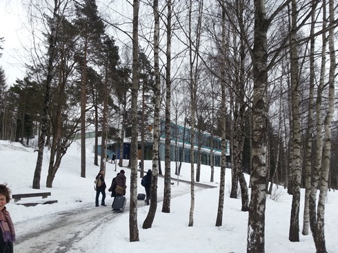 Group of people walking with suitcases through snowy woods to the National Archives building.