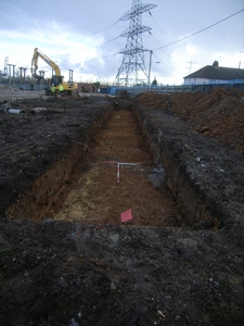 Partially excavated trench with digger in the background