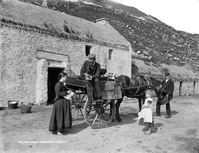 Black and white photo pf a man on a horse drawn cart talking to a women and child outside a thatched pub set against a rocky hillside