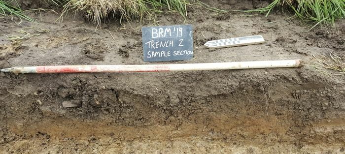 Photograph of a trench with writing on a chalk board. Could someone who is visually impaired access the written information? Image from: Archaeological Research Services Ltd (2020) Archaeological Works at Bakewell Road, Matlock, Derbyshire. https://doi.org/10.5284/1081998