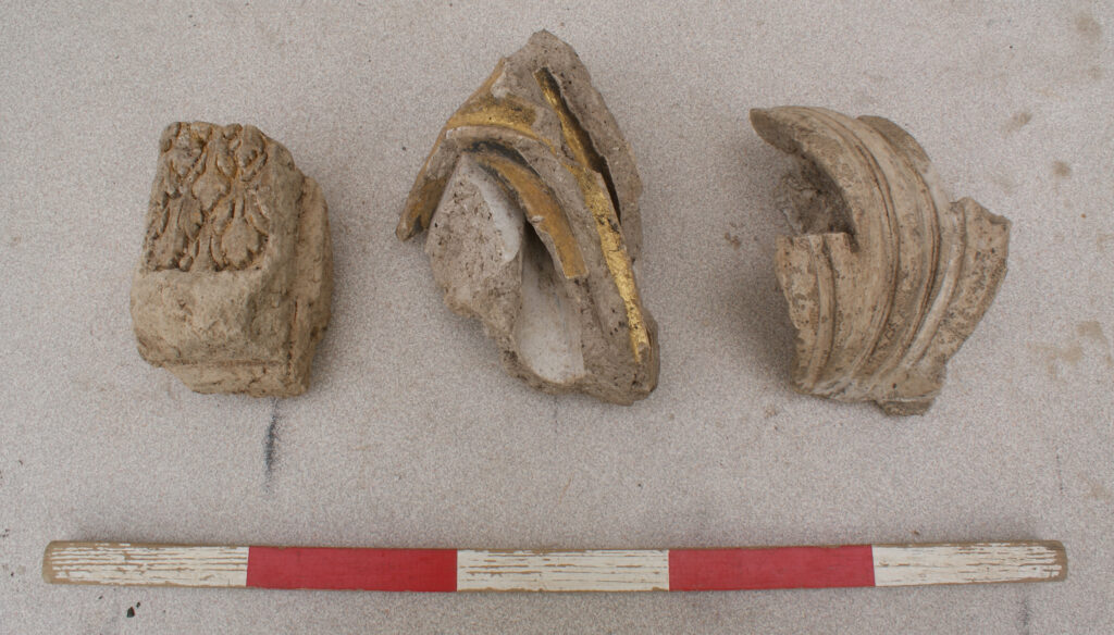 Photograph showing three plaster fragments with gold leaf, found during the excavation at Hardwick Park