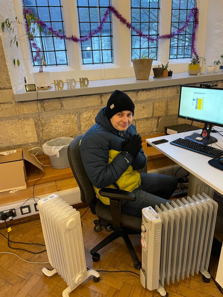 A picture of a ADS staff member in hat and coat surrounded by multiple electric heaters