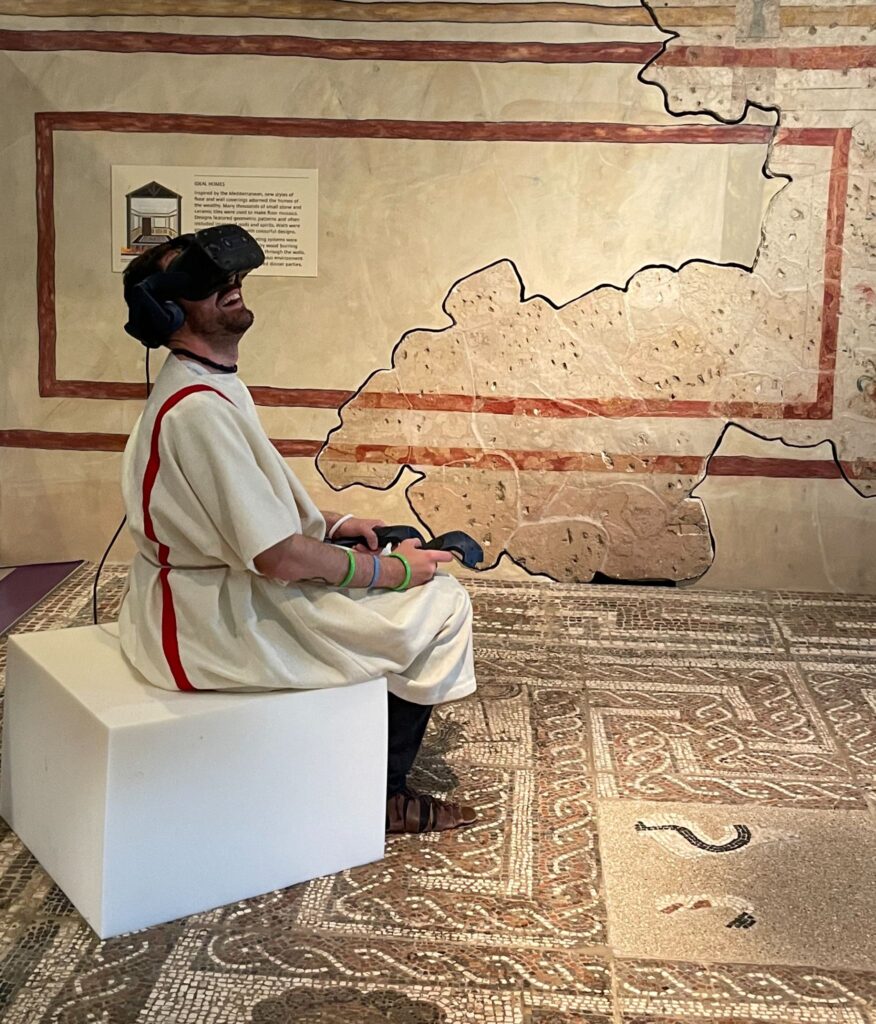 A picture of a person using a VR headset while dressed in Roman clothing in an appropriate setting