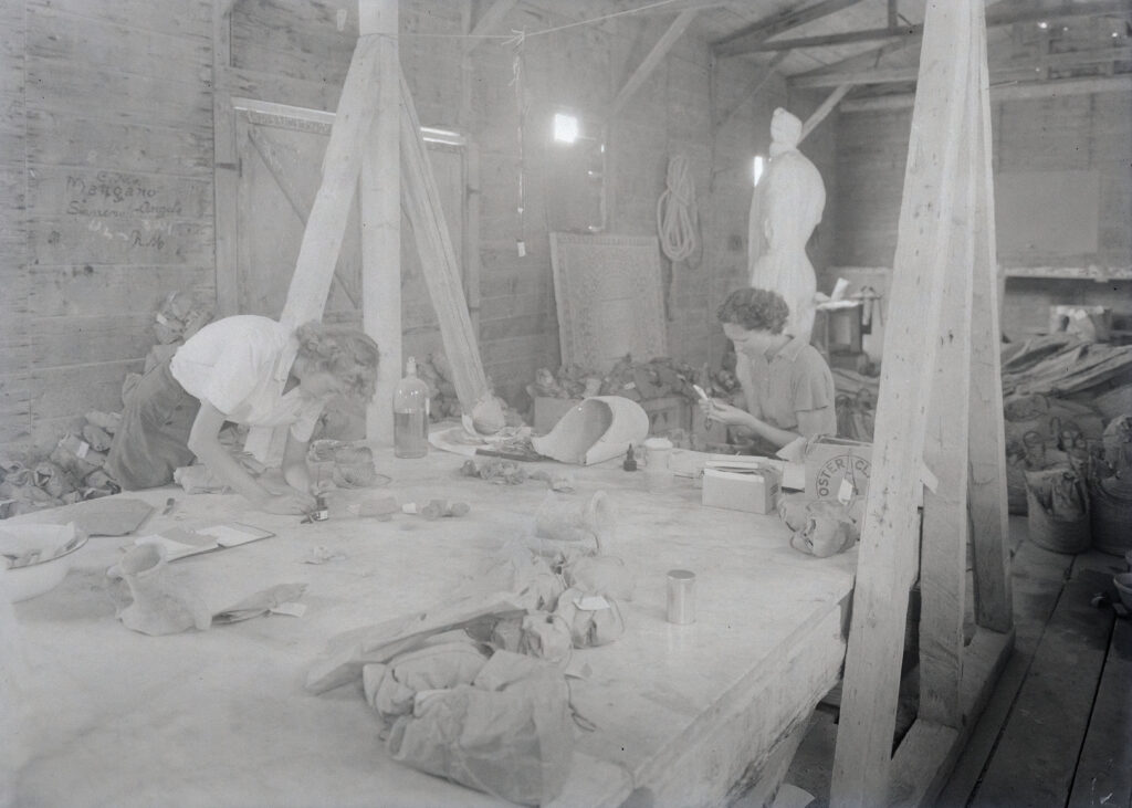 Black and white photo showing two women labelling artefacts