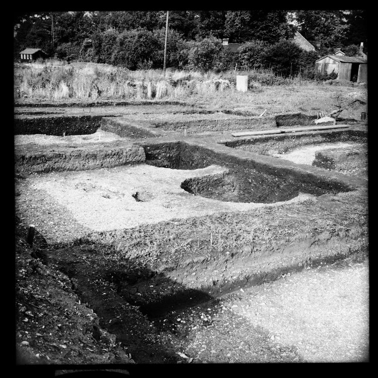 Black and white image showing a large excavation site with trees in the background 