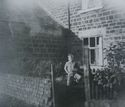Thumbnail of Black and white photograph, c.1950s, showing child standing outside Colliery House, next to Cruck Building. Handwritten text reads 