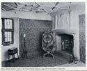Thumbnail of Black and white photograph showing furnished interior of room in Turret House, including fireplace, window, moulded ceiling, carpets and soft furnishings on chair. Text below the image reads 