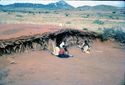 Thumbnail of Semi-subterranean tembe house with people seated outside