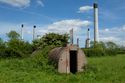 Thumbnail of 110497_HBR_Image_055, general view of an air raid shelter covered in vegetation growth within the Second World War site, with an industrial power station in the background.