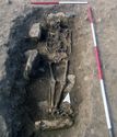 Thumbnail of Figure 3.211: Bainesse Cemetery: prone skeleton in cist 13085 in Grave 237, showing reused armchair voussoirs at the head and feet.